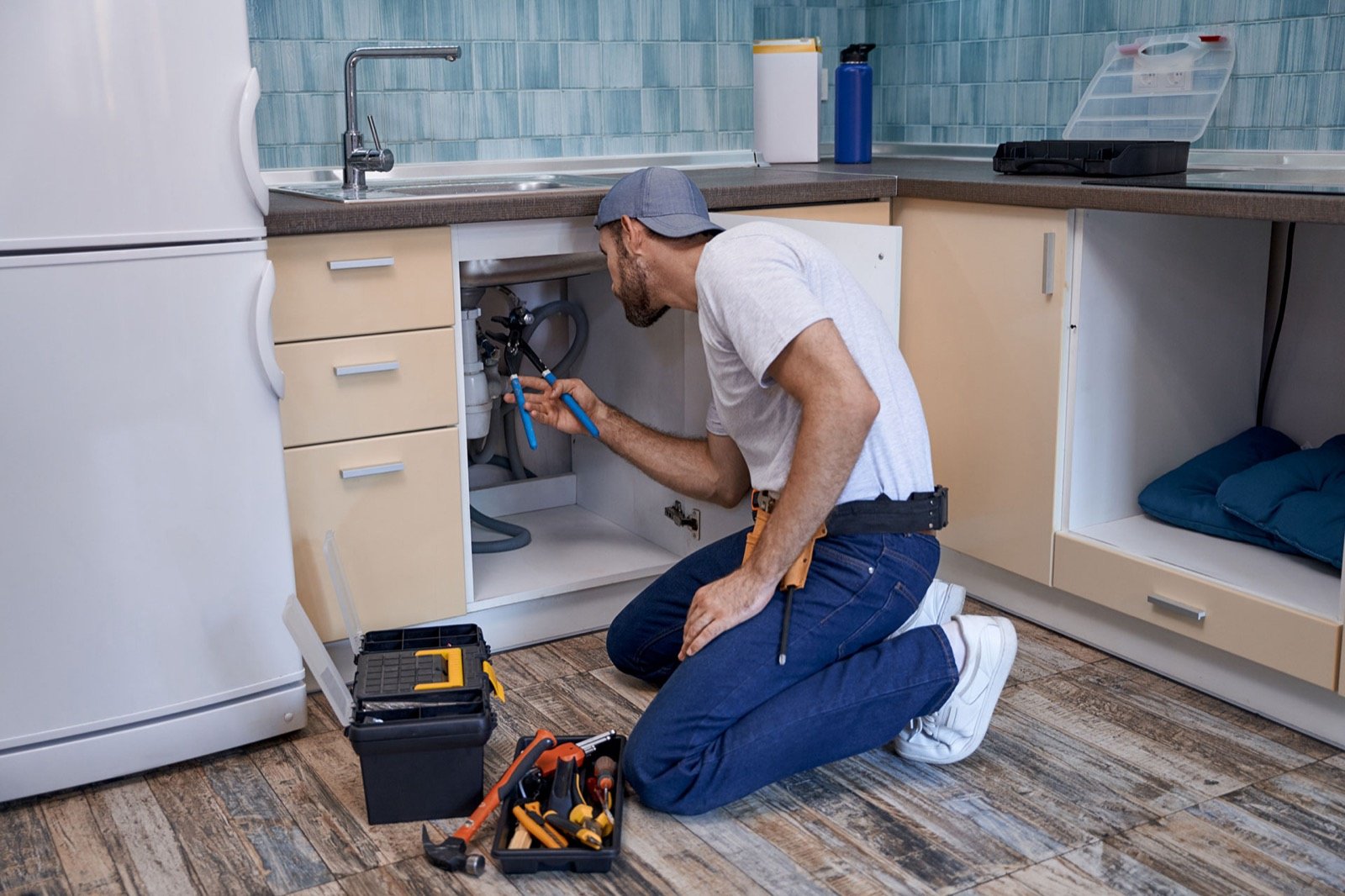 A plumber fitting pipes under a kitchen counter
